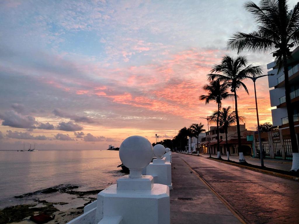 Sonnenuntergang über dem Wasser mit einer Statue auf einem Bürgersteig in der Unterkunft Hostel Auikyani in Cozumel