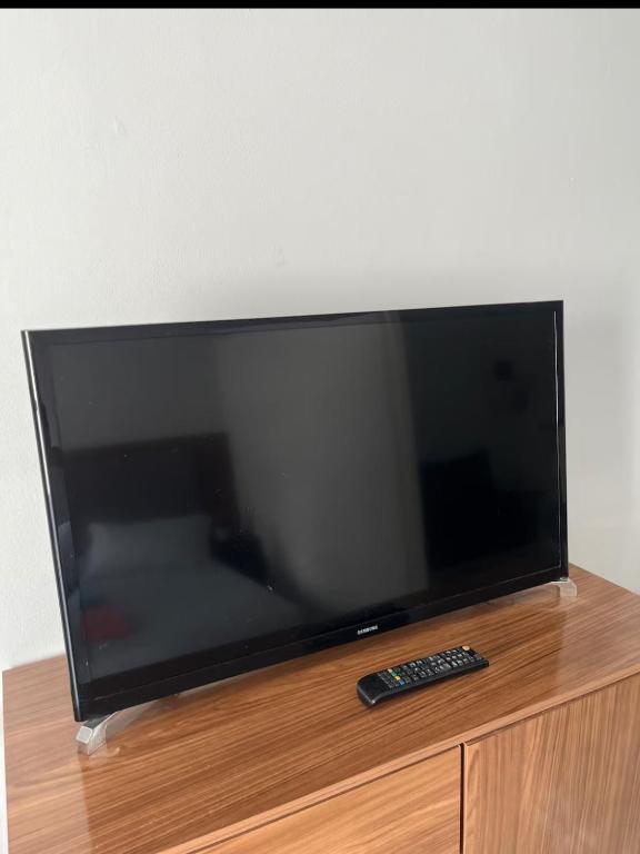 a flat screen tv sitting on a wooden stand with a remote control at Bela vista jardim camburi in Vitória
