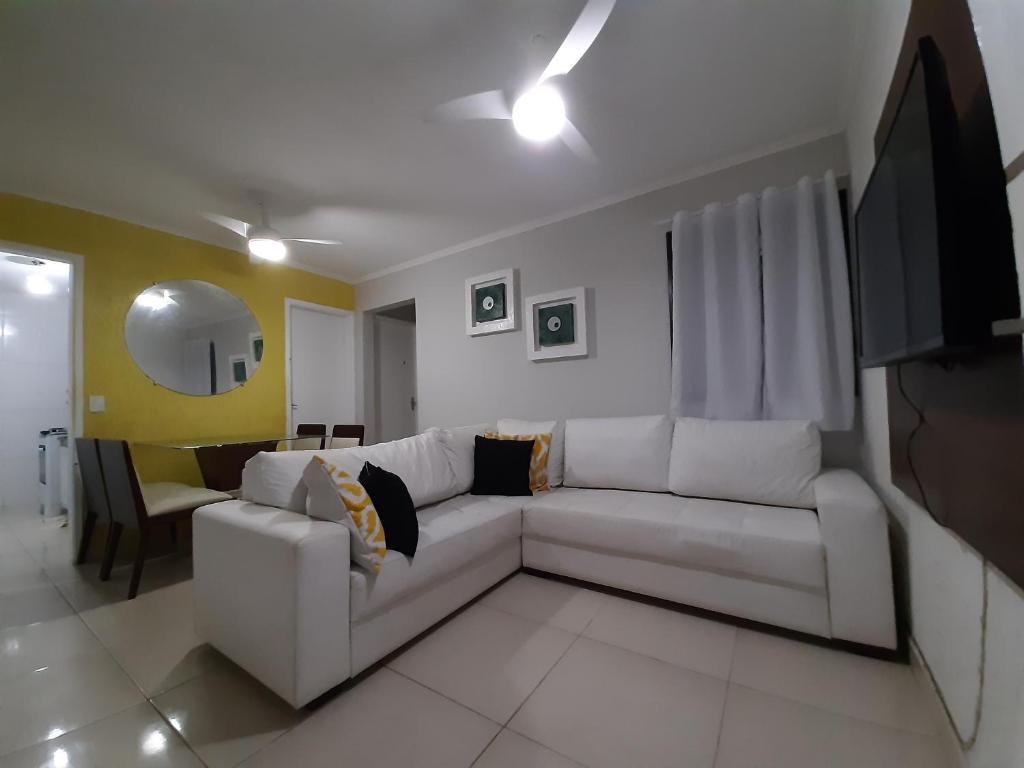 ein Wohnzimmer mit einem weißen Sofa und einem Fernseher in der Unterkunft Bate & Volta - Apartamentos com 2 quartos próximo ao SESC Bertioga in Bertioga