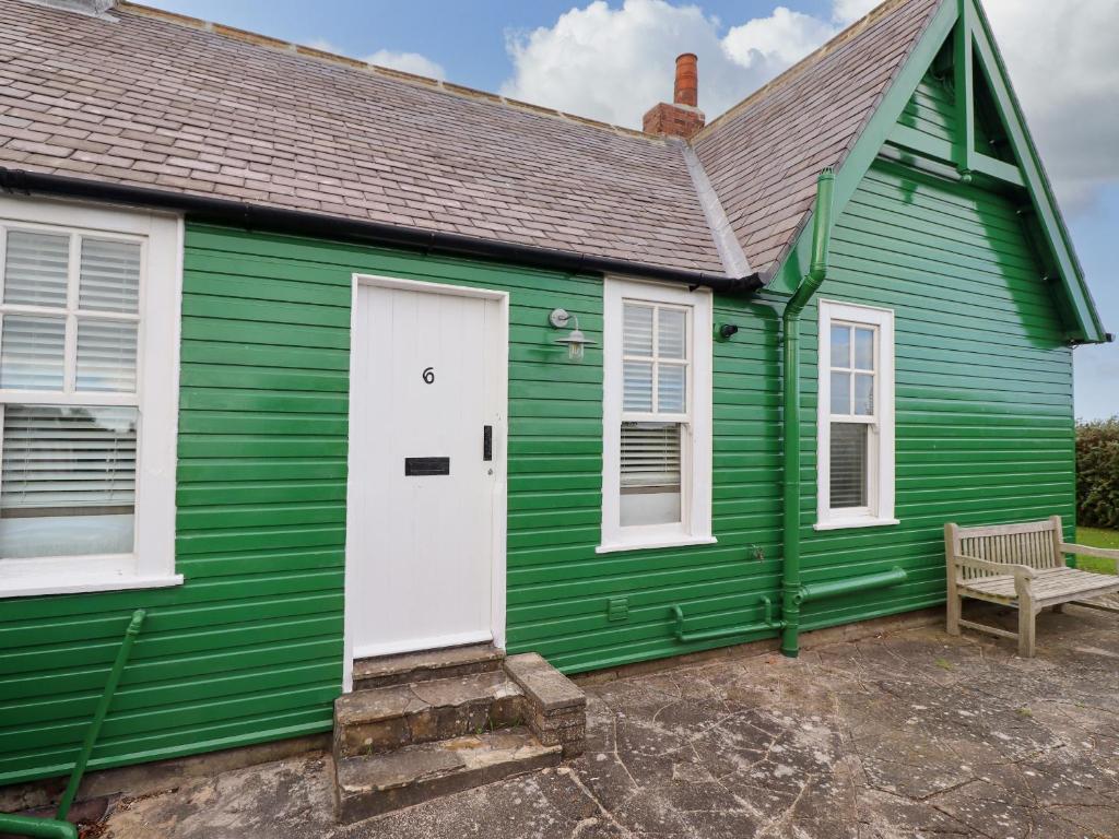 a green house with a white door and a bench at Armstrong Cottages No6 in Bamburgh