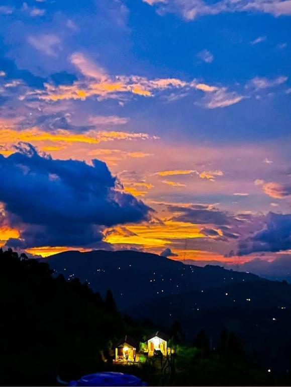 a sunset over a mountain with a house in the foreground at Lucknature Cabana Kandy in Elamalwewa