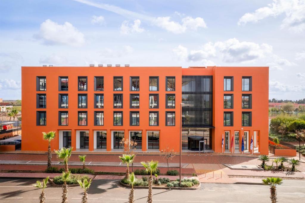 an orange building with palm trees in front of it at Hampton By Hilton Ben Guerir in Benguerir