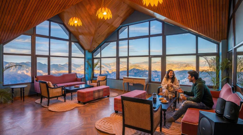 two people sitting in a room with huge windows at Zostel Kufri in Kūfrī