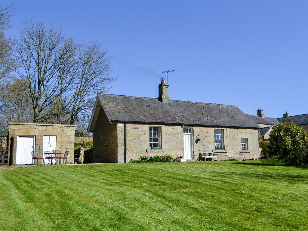 an old stone house with a large grass yard at Keepers Cottage Burradon in Sharperton