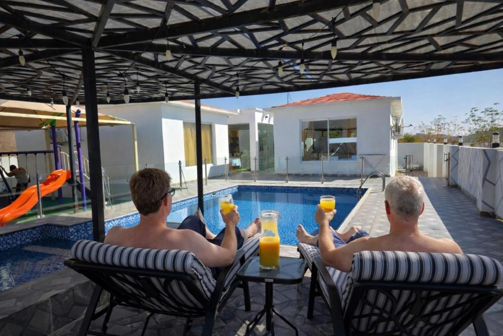 two men sitting in chairs drinking orange juice by a pool at Wadi Bani Khalid - Al Joud Green Hostel in Zilaft