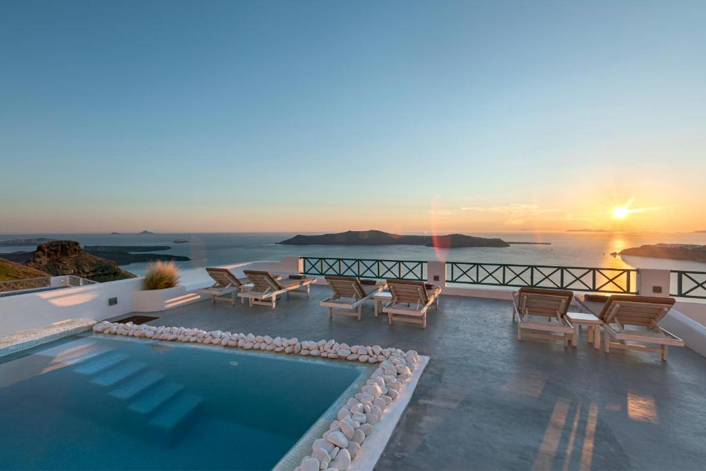 a pool with chairs and a sunset in the background at Afroessa Hotel by Caldera Houses in Imerovigli