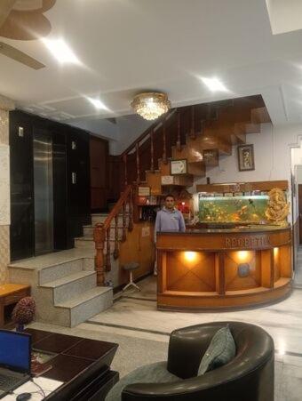 a man standing behind a counter in a room with stairs at Hotel Anmol in Dehradun