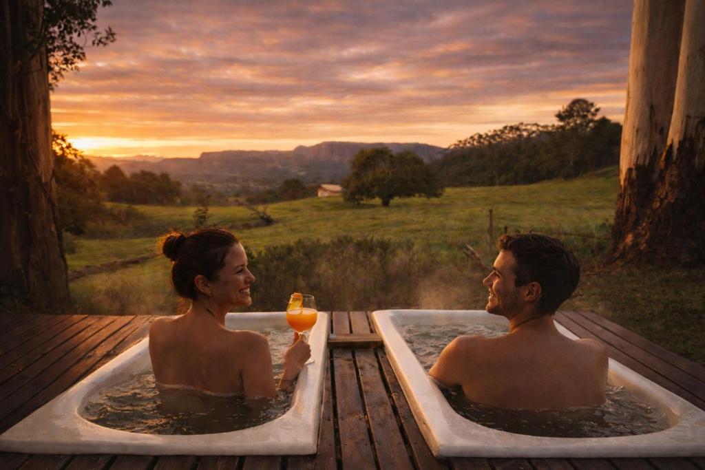 a man and woman in a bath tub with a glass of wine at Cabana estilo Glamping com Banheiras Quente e Vista às Montanhas in Rio do Sul
