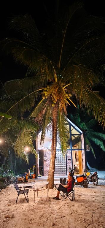 a person sitting in a chair under a palm tree on the beach at Sekinchan Tiny House - Moslim Only in Sekinchan