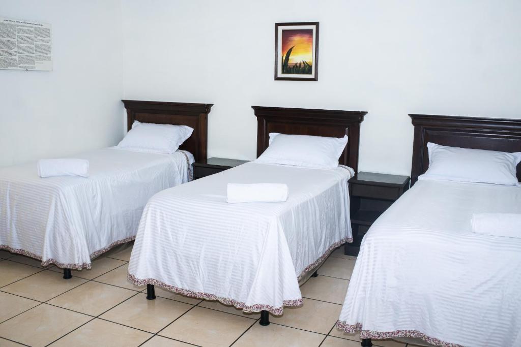 three beds in a room with white sheets at Hotel Pablo Tesák in San Vicente