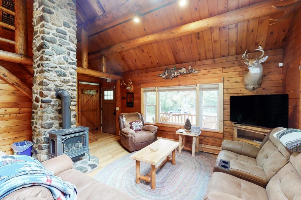a living room with a stone fireplace in a log cabin at Wooded Family Retreat! 11 Mi to Acadia Entrance in Trenton