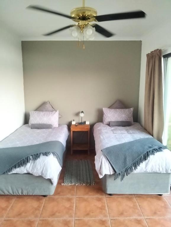 two beds in a room with a ceiling fan at Golden Mile Estate Self Check Inn in eMalahleni