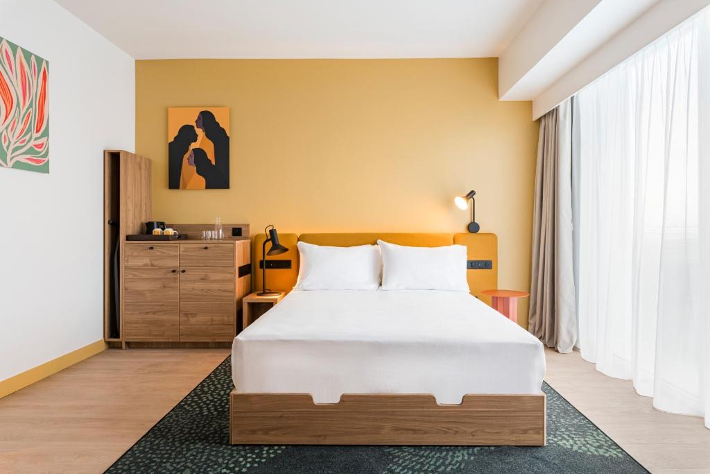 a bedroom with a large white bed and a dresser at Hampton by Hilton Bordeaux Merignac Airport in Mérignac