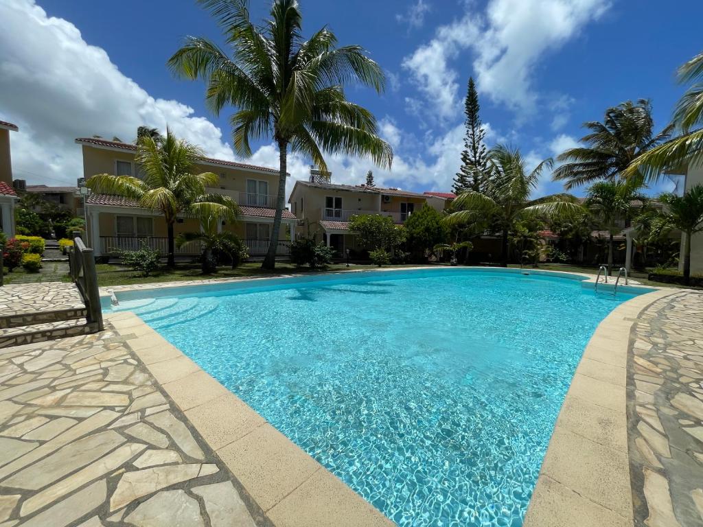 a swimming pool with palm trees and a building at Cozy 3BR Duplex with Pool & Garden View - Grand Gaube Getaway in Grande Gaube