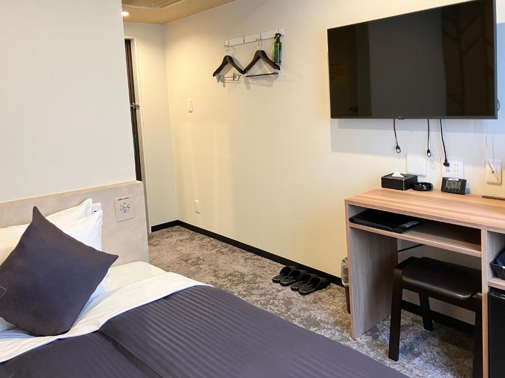 a bedroom with a bed and a desk with a television at HOTEL LiVEMAX BUDGET Chofu-Ekimae in Chofu