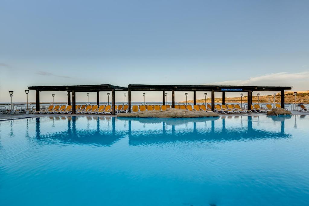 una grande piscina di acqua blu con sedie e un edificio di AX Sunny Coast Resort & Spa a San Pawl il-Baħar