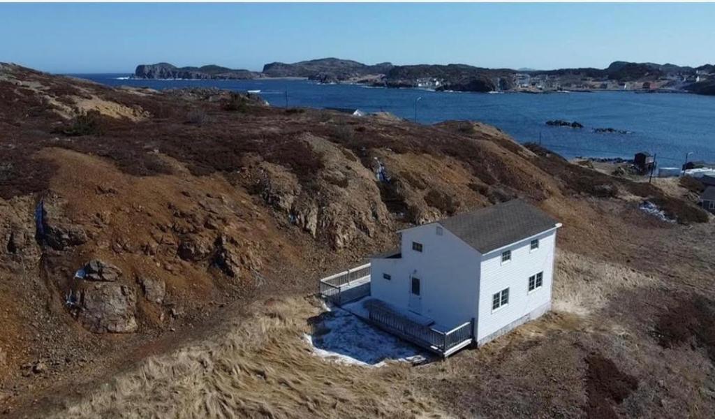 a small white house on a hill next to the water at Salty B'y Cottage in Twillingate