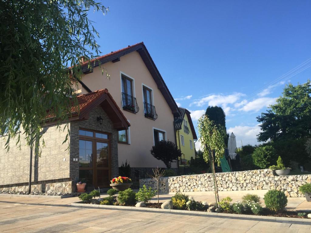 a white house with a stone wall and a fence at Penzion Werbew in Vrbov