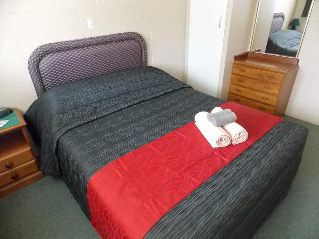 1 dormitorio con 1 cama con manta roja y espejo en Rangiora Lodge Motel en Rangiora