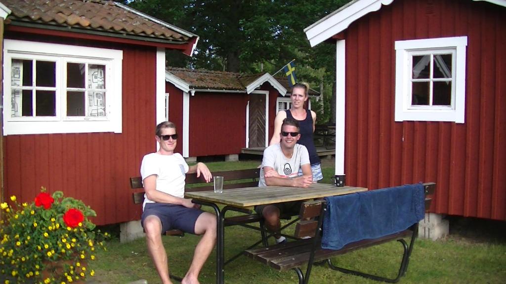 three people sitting at a table in front of a red shed at Visingsöstugorna in Visingsö