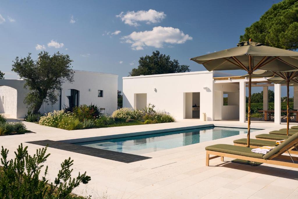 a swimming pool with two lounge chairs and an umbrella at Masseria Pietra e Terra in Carovigno