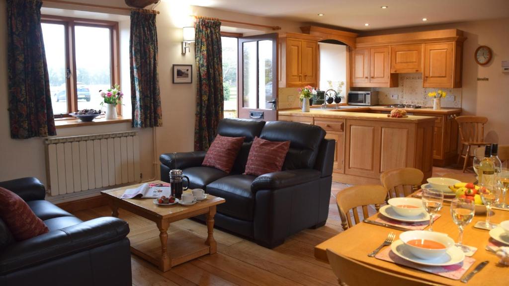 a living room with black leather furniture and a kitchen at Knightcote Farm Cottages in Gaydon