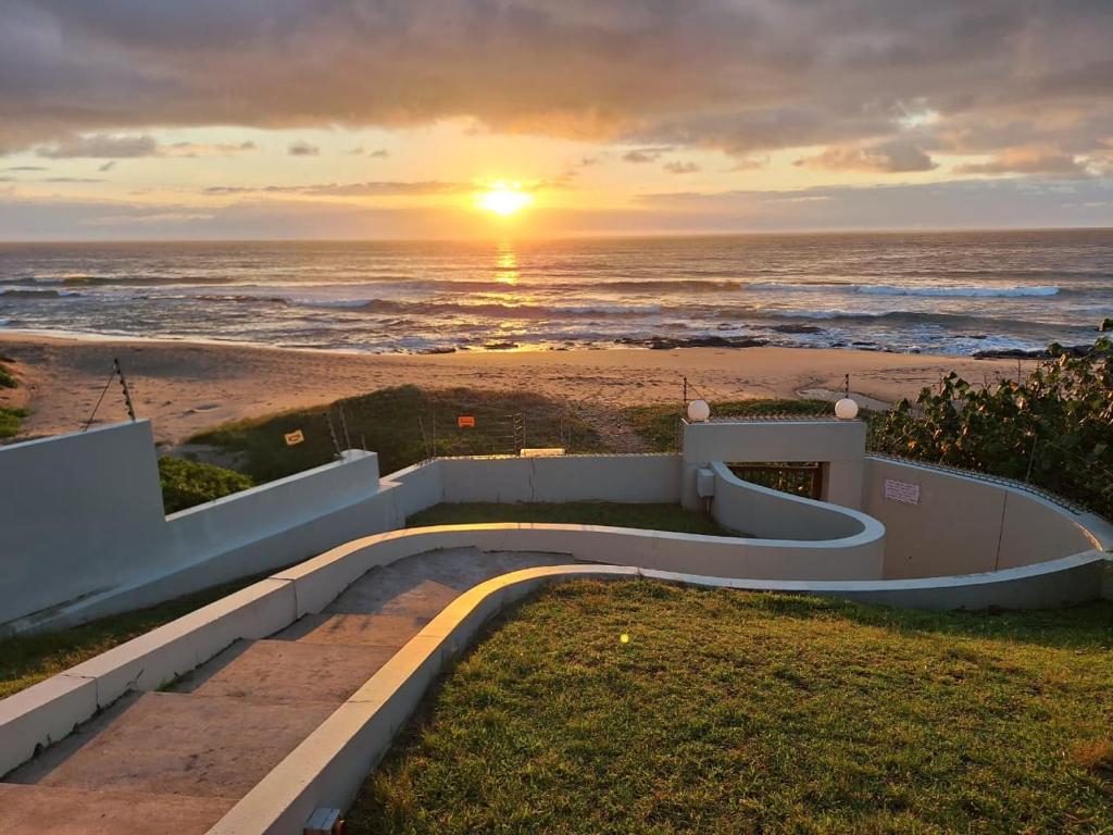 a sunset over the ocean with a path leading to the beach at Shore Breakers in Shelly Beach