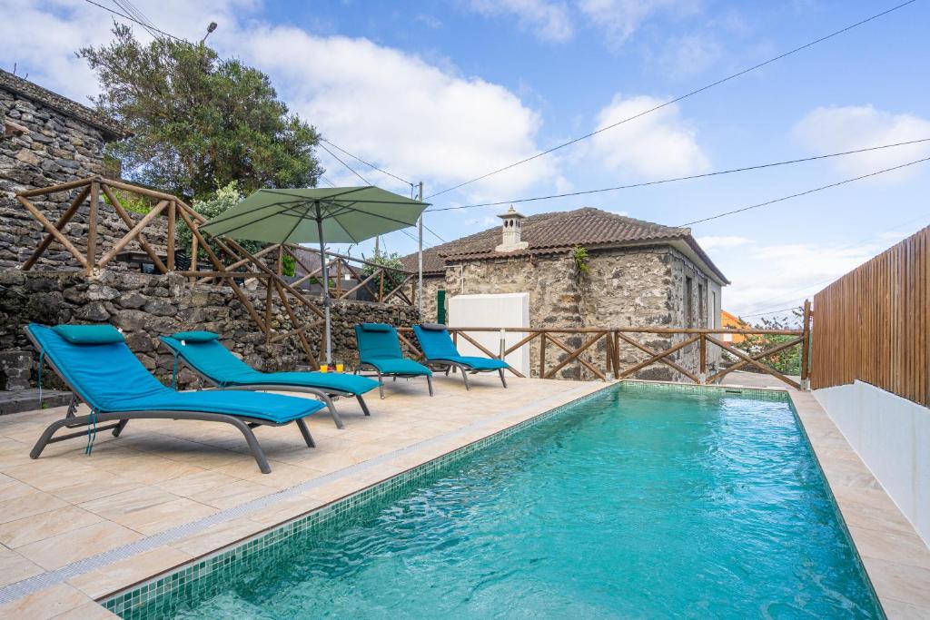 a swimming pool with blue chairs and an umbrella at Gouveia Cottage in Seixal