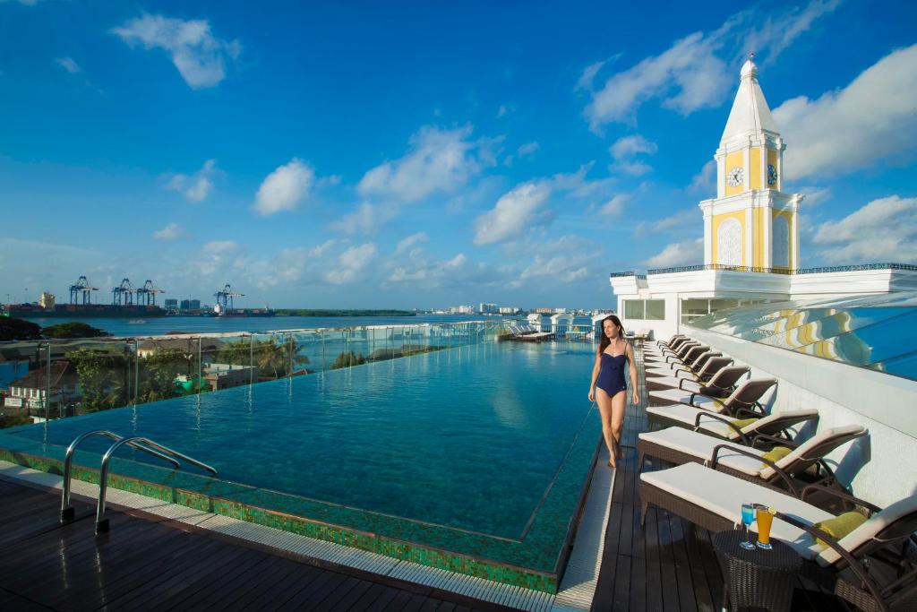 Eine Frau steht auf dem Balkon eines Hotels mit einem Uhrturm in der Unterkunft Fragrant Nature Kochi - A Five star Classified Hotel in Kochi