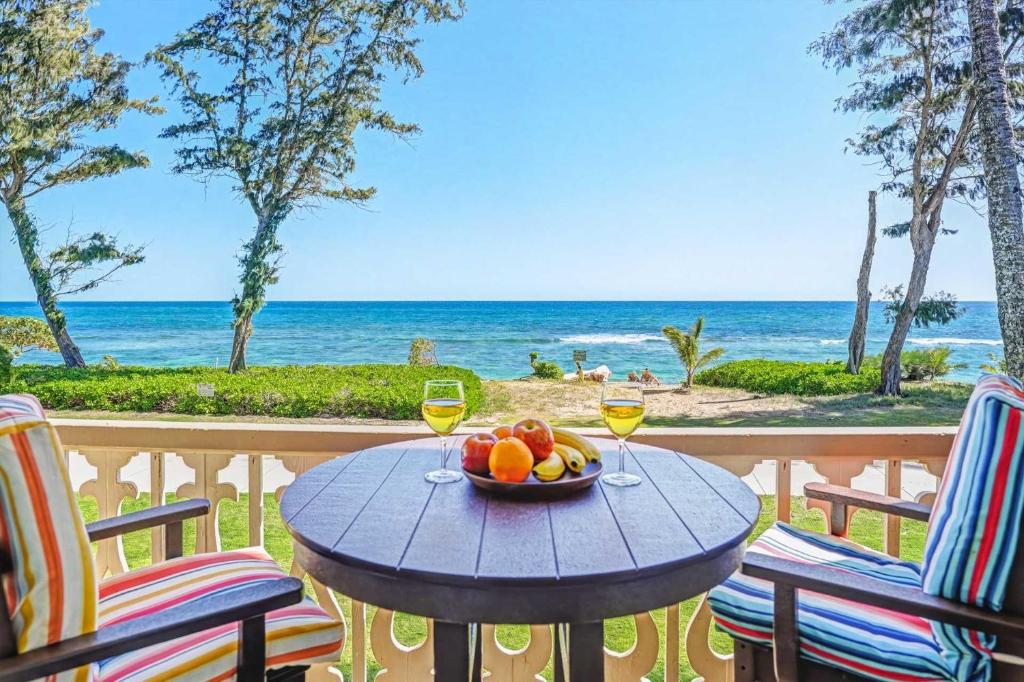 a table with a bowl of fruit and two glasses of wine at Islander on the Beach 249 in Kapaa