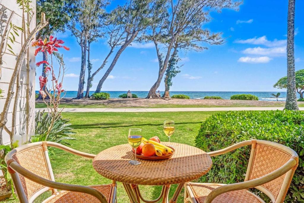 a table with a bowl of fruit and two glasses of wine at Islander on the Beach 131 in Kapaa