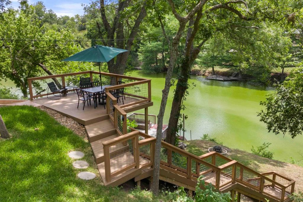 a deck with a table and an umbrella next to a river at Stunning Rivrefront 3BR with Hot tub, water view! in Seguin