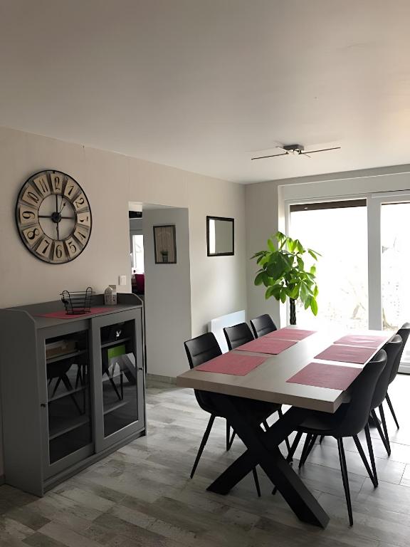 a dining room with a table and chairs and a clock at Gîte Les Aubennes in Fromelennes