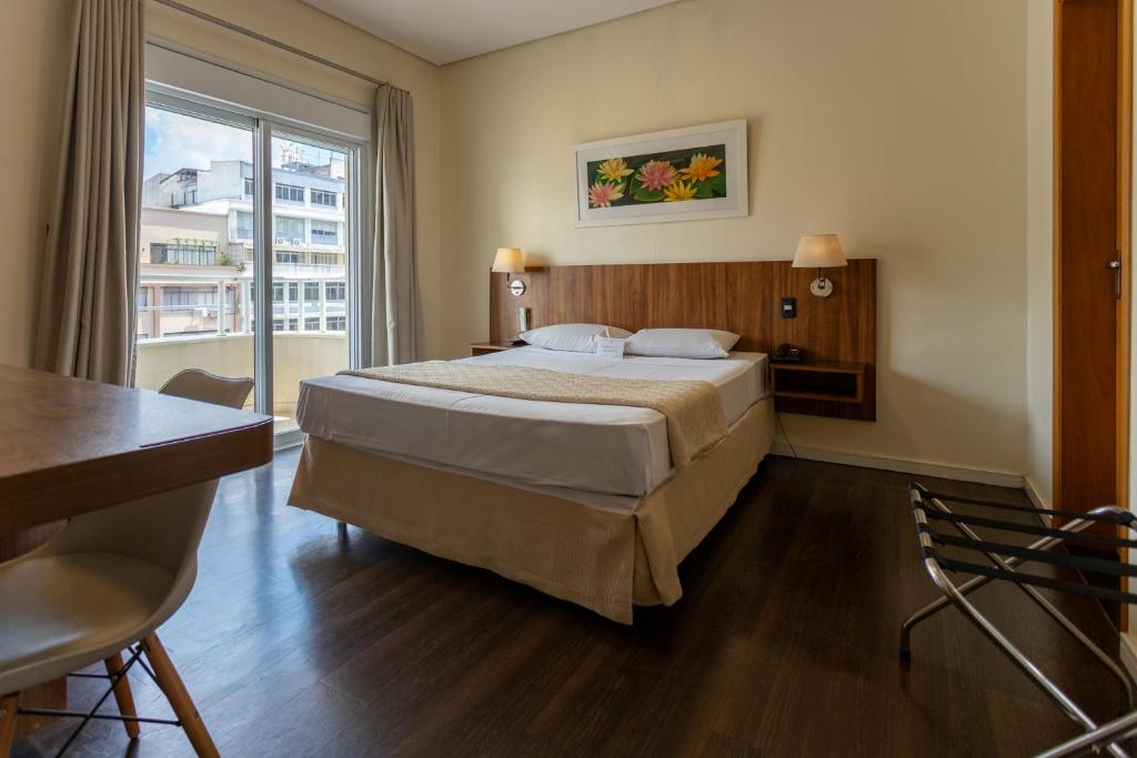 a bedroom with a bed and a desk and a window at Hotel Amalia by Plaza Xavier in São Paulo