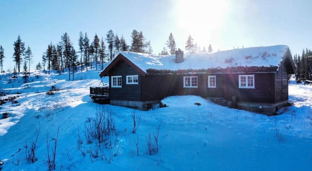 a house is covered in snow with the sun behind it at Idyllisk feriested in Gol