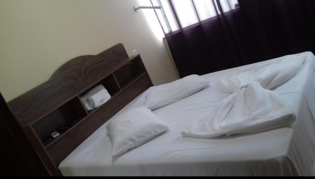 a bed with white sheets and pillows on it at Hotel Mourão in Guanhães