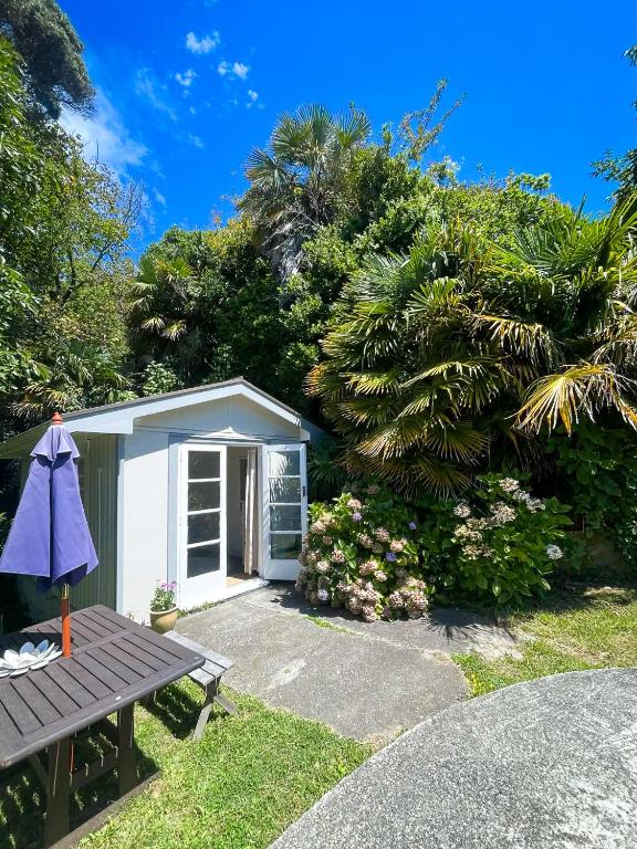 a small white shed with a picnic table and a tree at Ruby Bay Beach Sleepout - 30 mins from Abel Tasman in Mapua