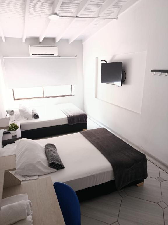 two beds in a white room with a tv at La Carpita Hotel in El Poblado