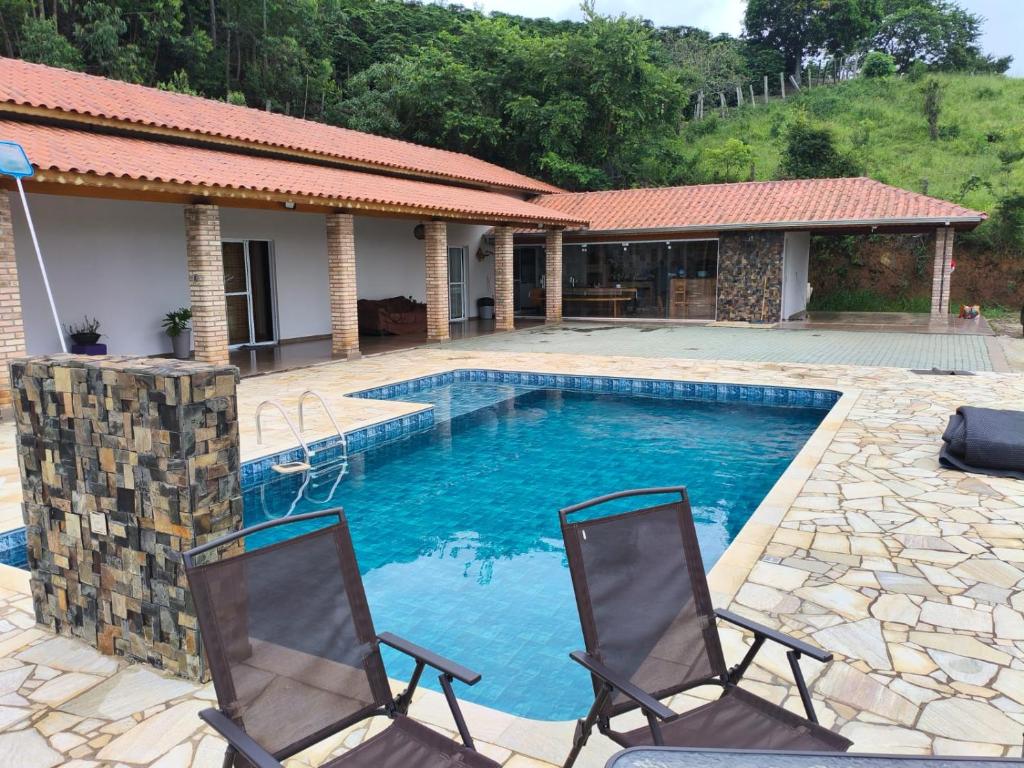 a swimming pool with two chairs in front of a house at Chácara Lari & Sapão in Socorro