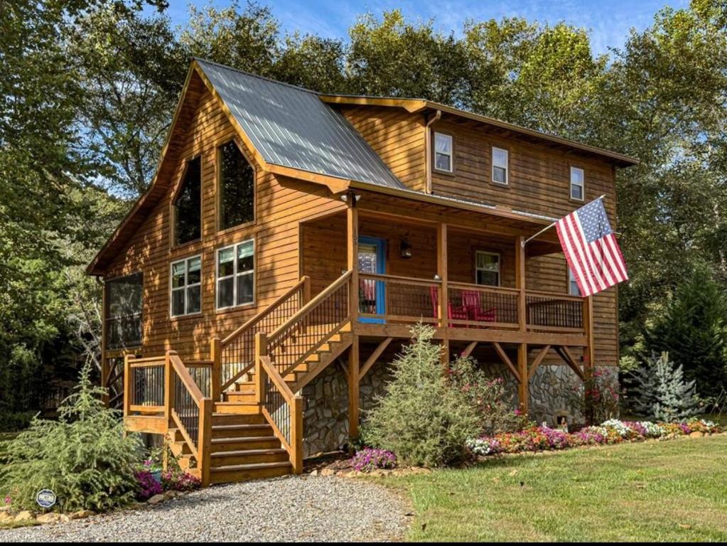 a log cabin with a porch and an american flag at Riverfront Blue Jay Cabin in Murphy