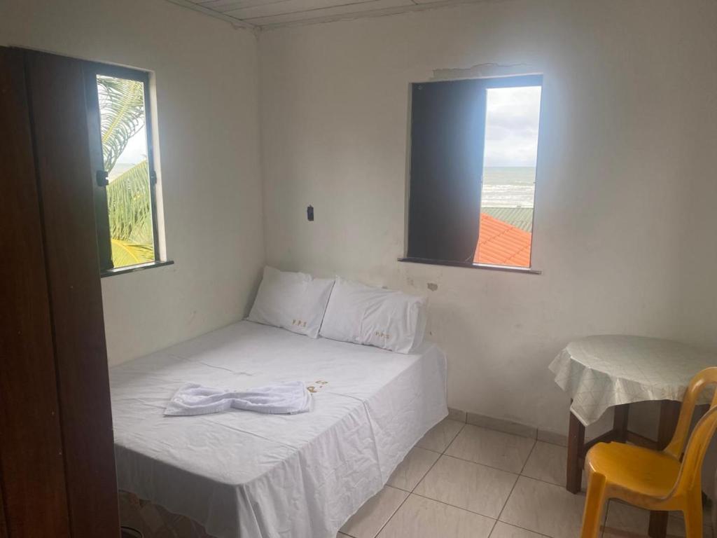 a small bedroom with a bed and a table and two windows at Cabana Maktub in Uruçuca