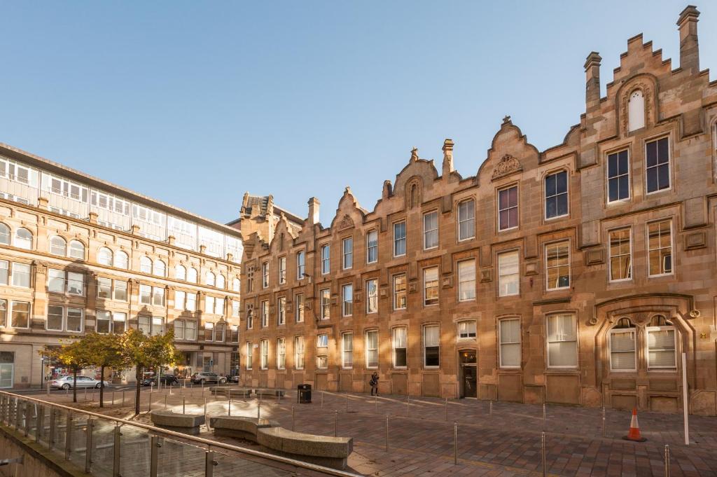 un gran edificio de ladrillo con bancos delante en Glasgow City Flats - Merchant City, en Glasgow