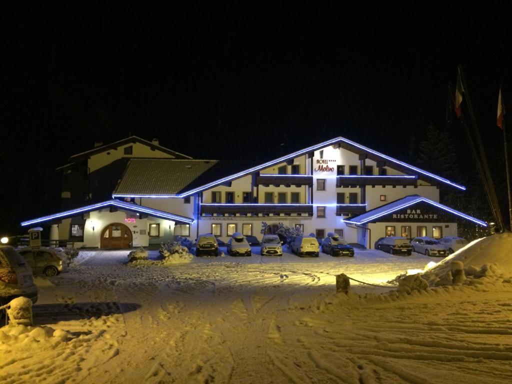 a hotel with cars parked in the snow at night at Hotel Molino in Falcade