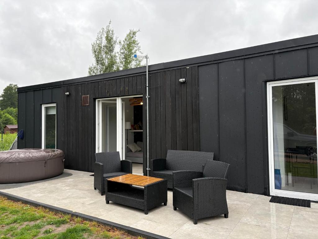 a black house with chairs and a table on a patio at Domek nad Strugą przy stawach 10 km od Warszawy" Jacuzzi na zamówienie" in Halinow