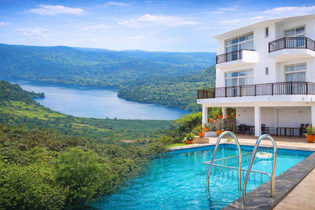 a swimming pool in front of a building with a view of a lake at HEMGIRI - Private Pool Villa Mulshi in Mulshi