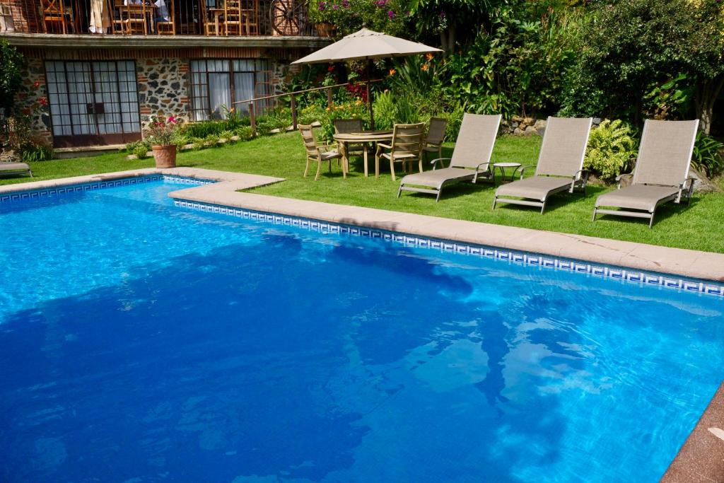 a swimming pool with chairs and a table and an umbrella at Hotel Casa del Angel in Tepoztlán