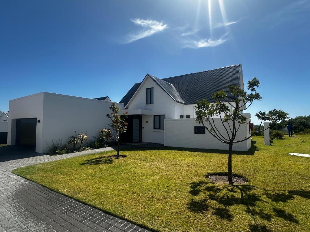 a white house with a tree in the front yard at Seabreeze Golf Retreat in St Francis Bay