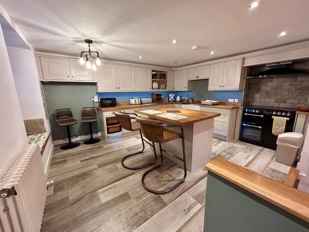 a kitchen with white cabinets and a island with chairs at Bakers Cottage in Cockermouth