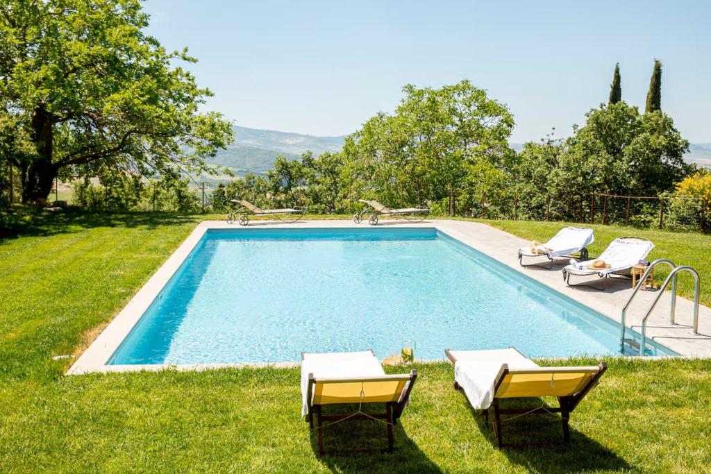 a swimming pool in the grass with two chairs at Villa Beltramonto by MMega in Castiglioncello del Trinoro