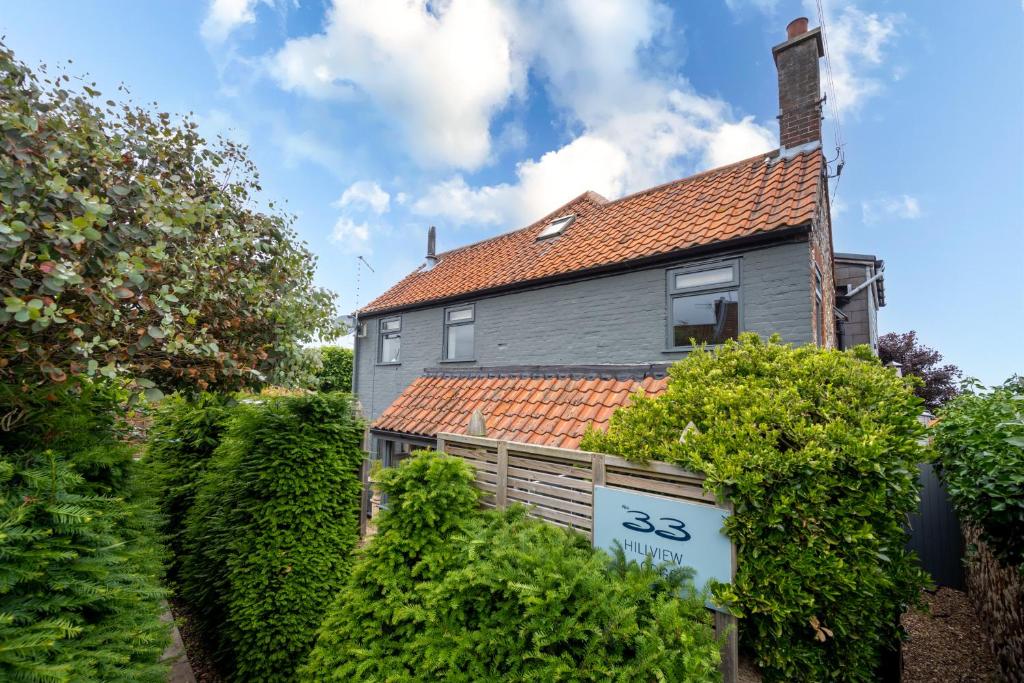 a gray house with a red roof and bushes at No33 HILLVIEW LODGE BOUTIQUE COTTAGE in Brancaster